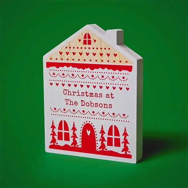 Personalised house-shaped Christmas decoration featuring festive red patterns and a custom family name on a white wooden plaque.